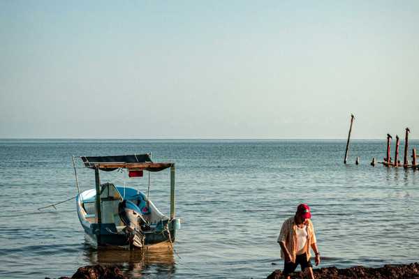 a man sitting on the shore of a beach next to a boat.
