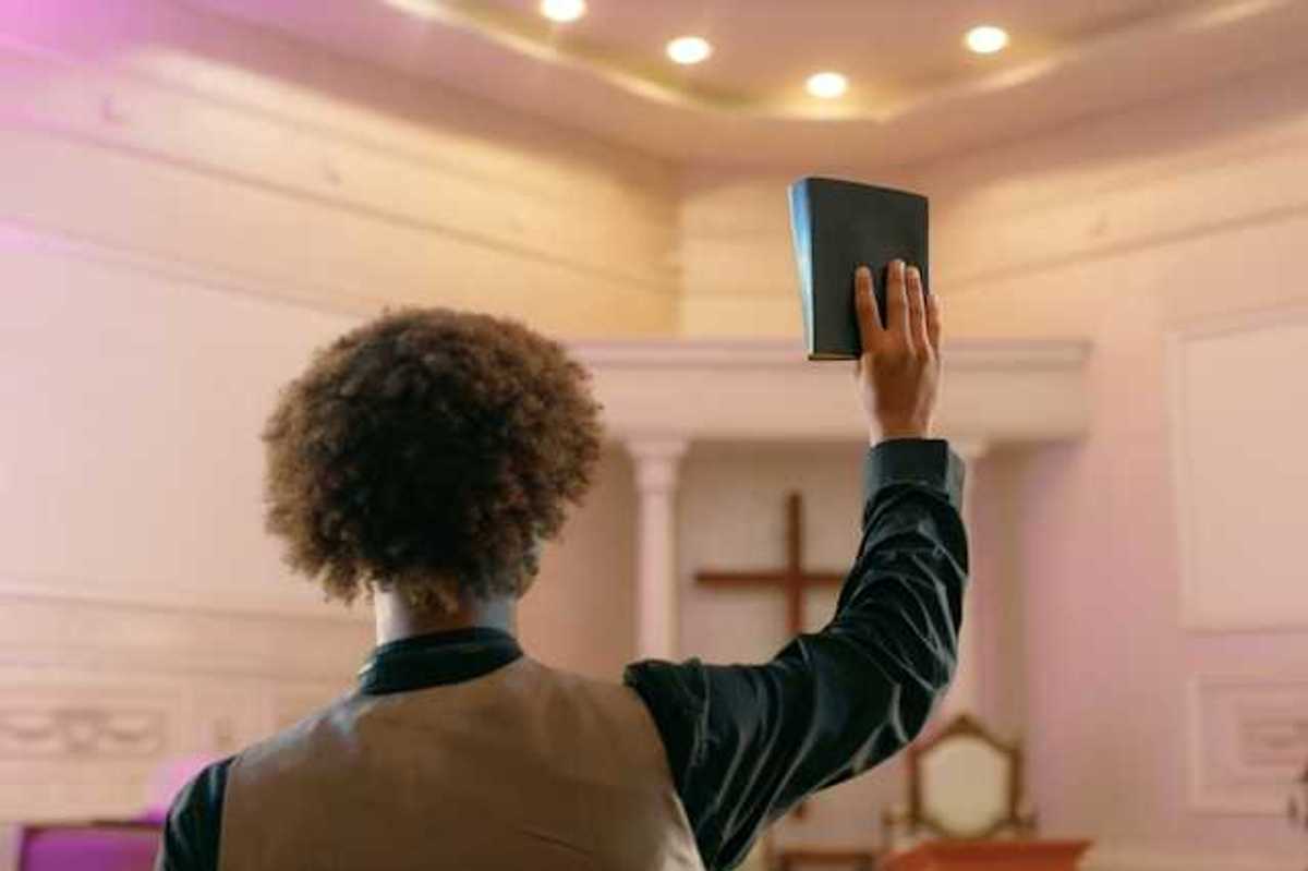 A man standing facing a Christian cross with a book raised in his right hand