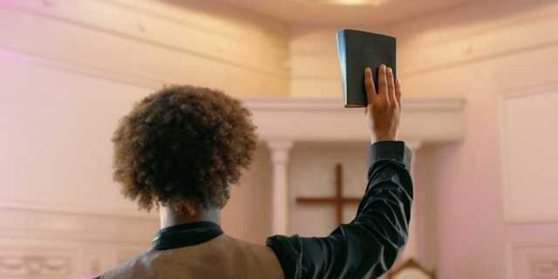 A man standing facing a Christian cross with a book raised in his right hand