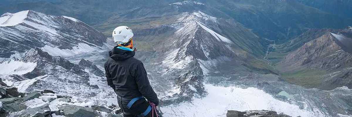A man standing on a peak looking out over a snowy mountainous landscape