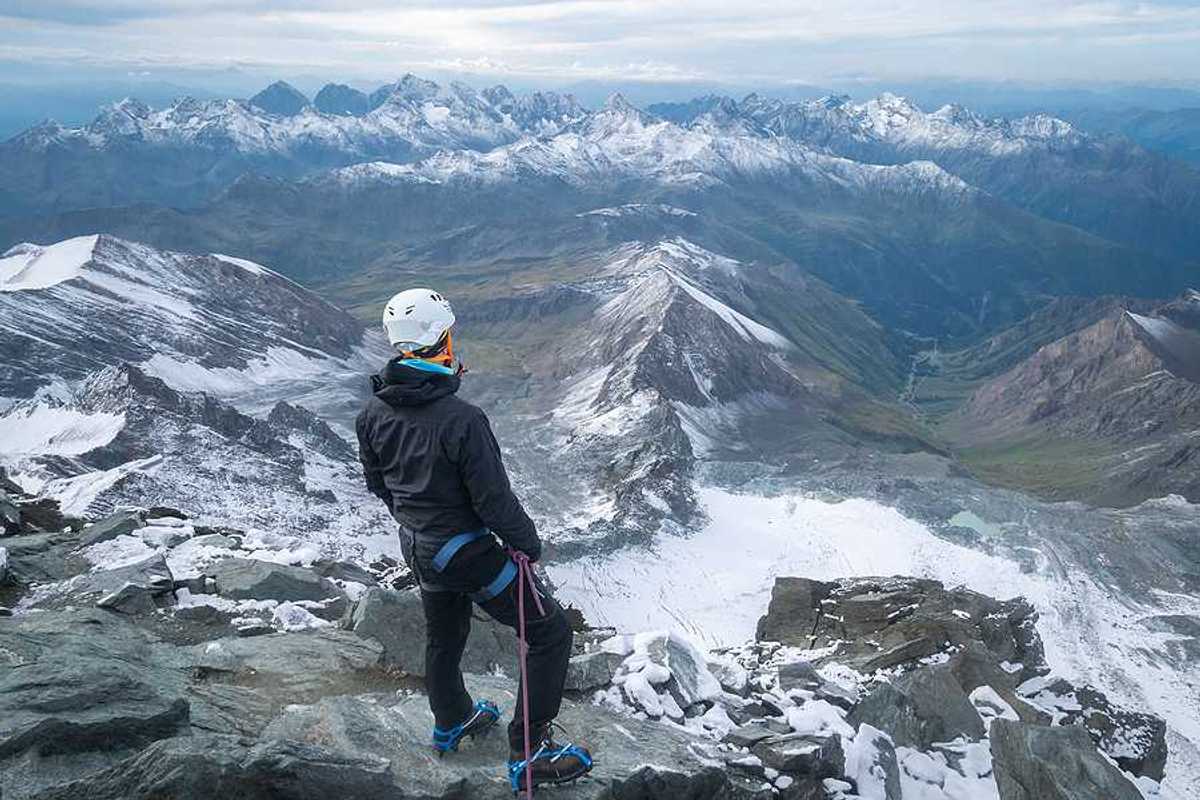 A man standing on a peak looking out over a snowy mountainous landscape
