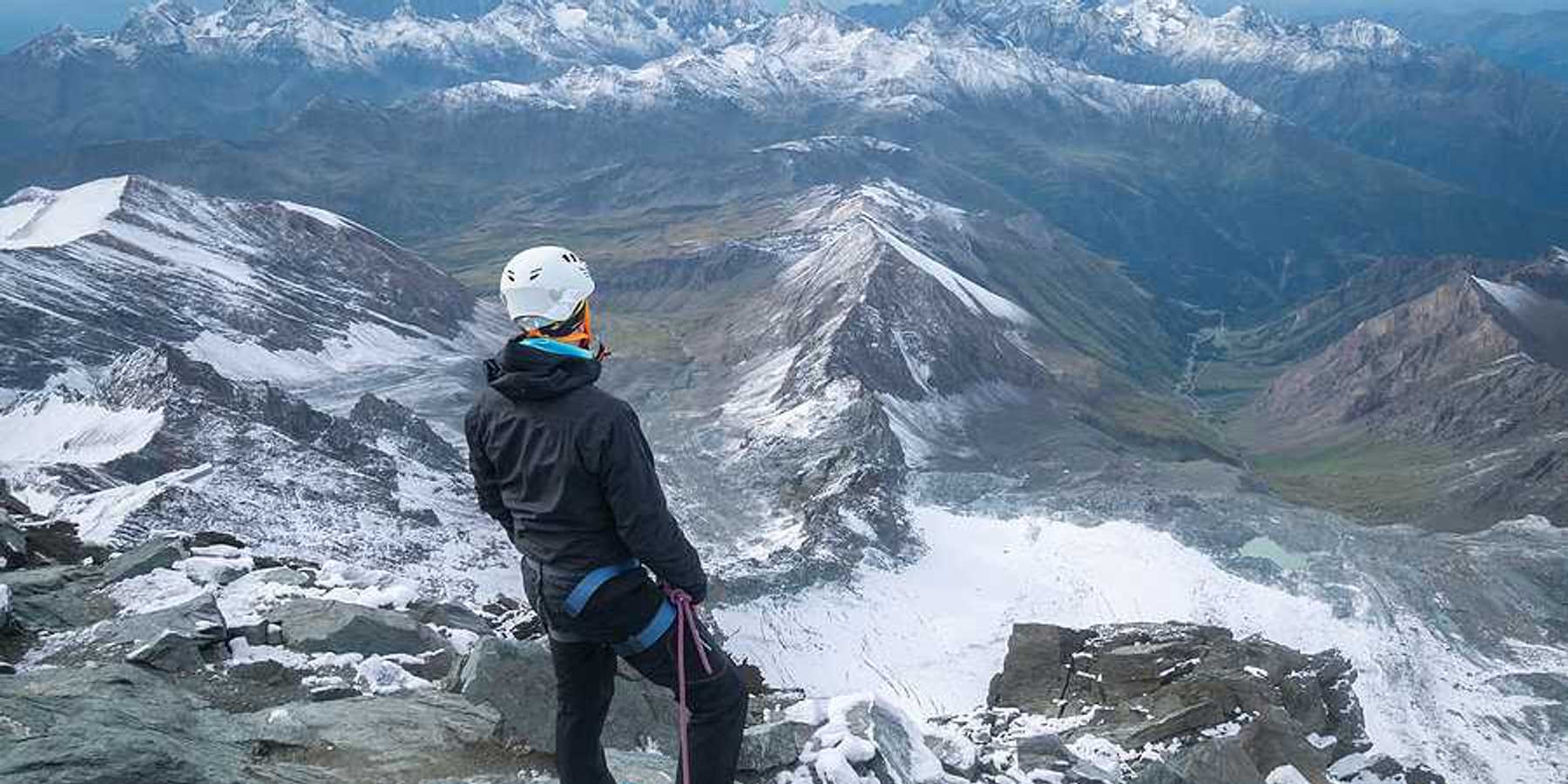 A man standing on a peak looking out over a snowy mountainous landscape