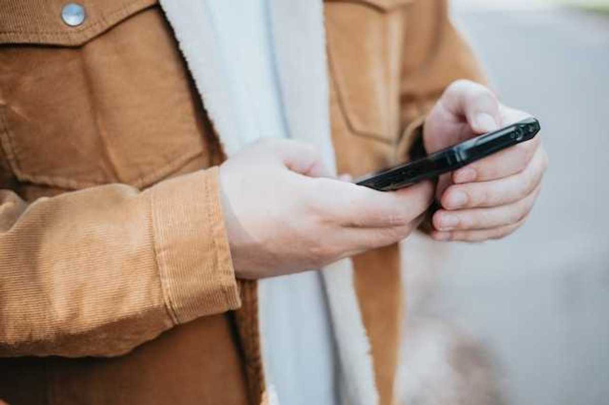 A man wearing a brown coat with his cell phone in his hands
