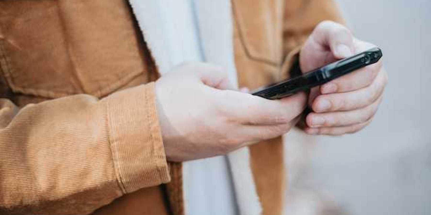 A man wearing a brown coat with his cell phone in his hands