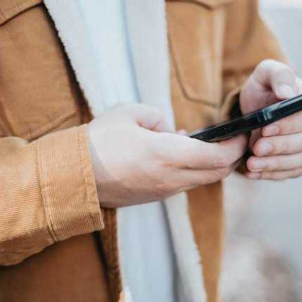 A man wearing a brown coat with his cell phone in his hands