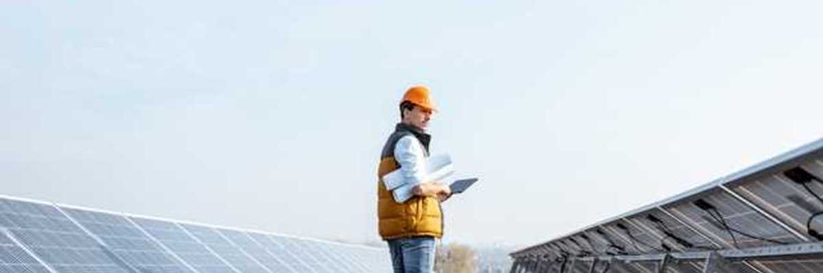 A man wearing a hardhat on a roof inspecting solar panels