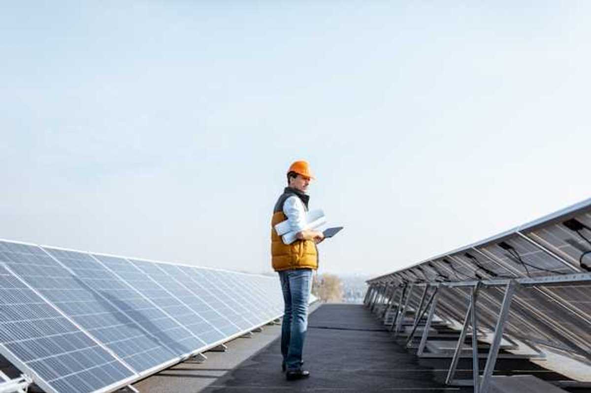 A man wearing a hardhat on a roof inspecting solar panels