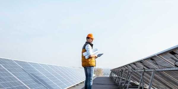 A man wearing a hardhat on a roof inspecting solar panels