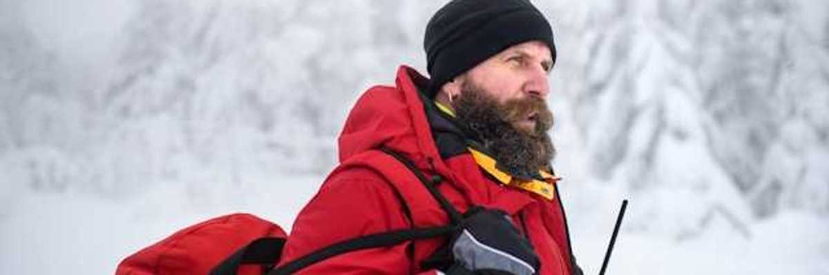 A man wearing a red jacket and carrying a red bag walking through a snowy landscape