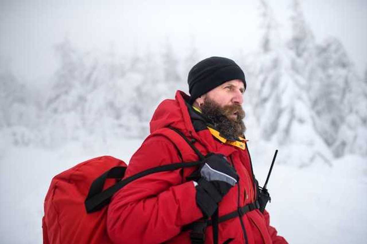 A man wearing a red jacket and carrying a red bag walking through a snowy landscape
