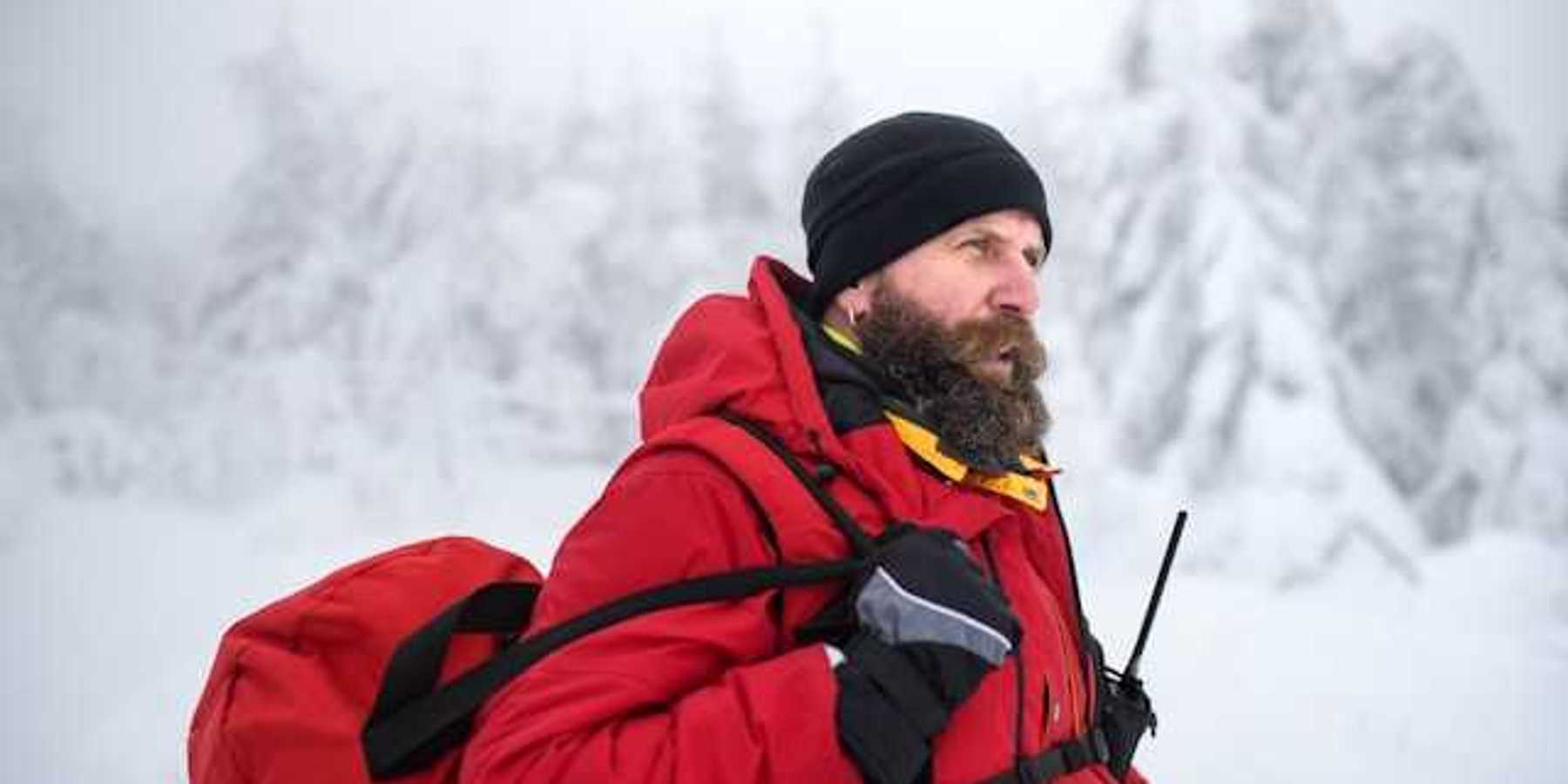 A man wearing a red jacket and carrying a red bag walking through a snowy landscape
