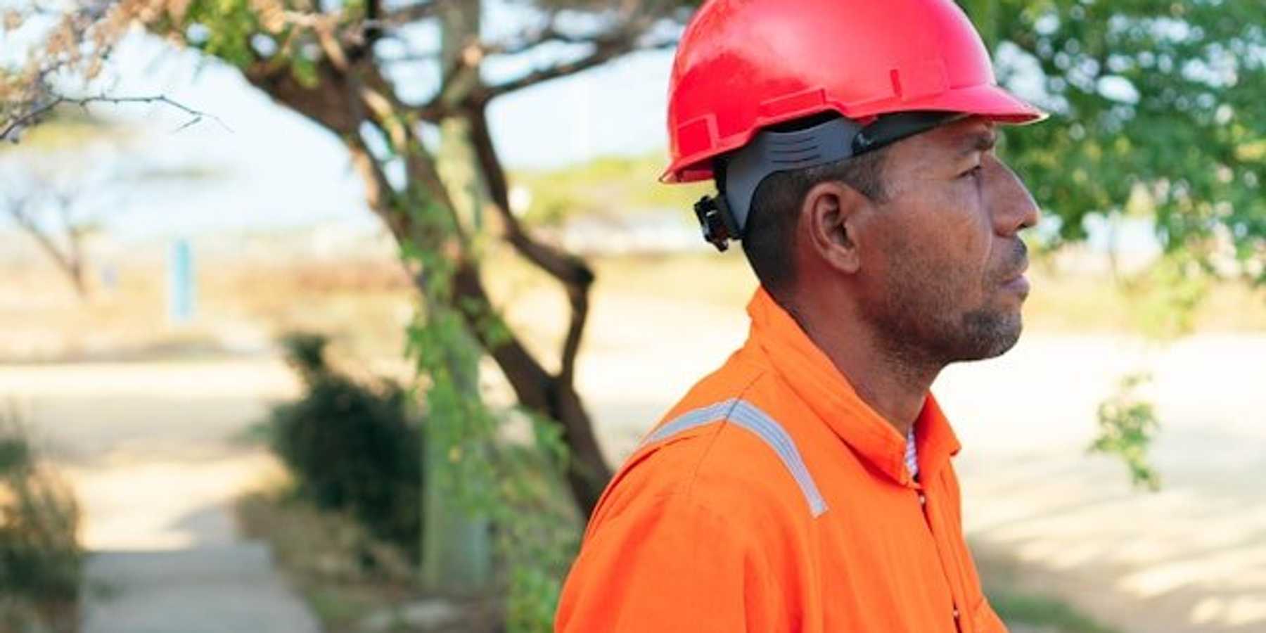 A man wearing an orange safety jumpsuit and hardhat on a sunny day.
