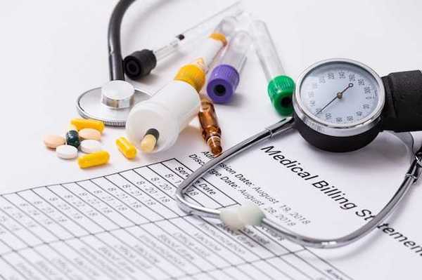 A medical billing statement with a stethoscope and assorted prescription pills next to it