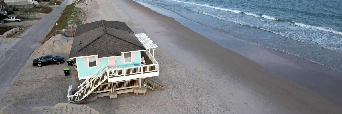 A mint-colored house on a beach sitting very close to the waves