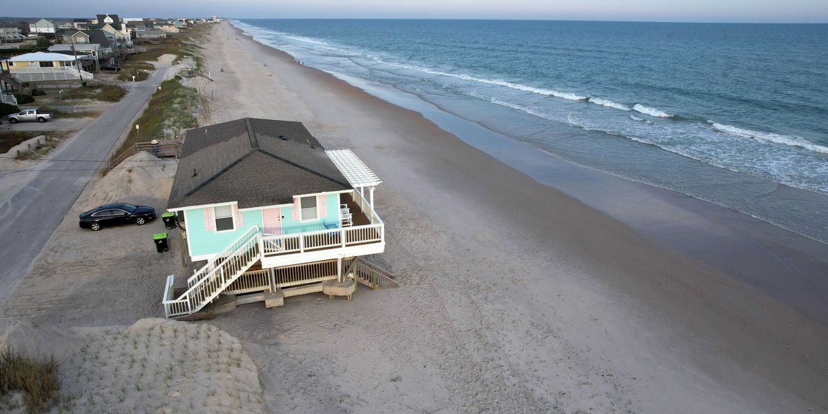 A mint-colored house on a beach sitting very close to the waves
