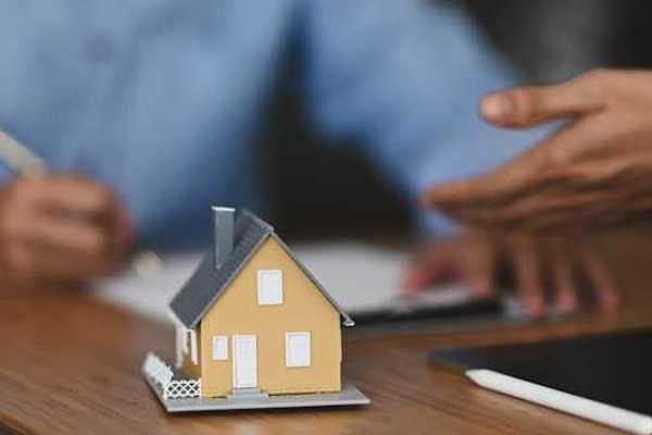 A model of a small house with two people signing paperwork in the background