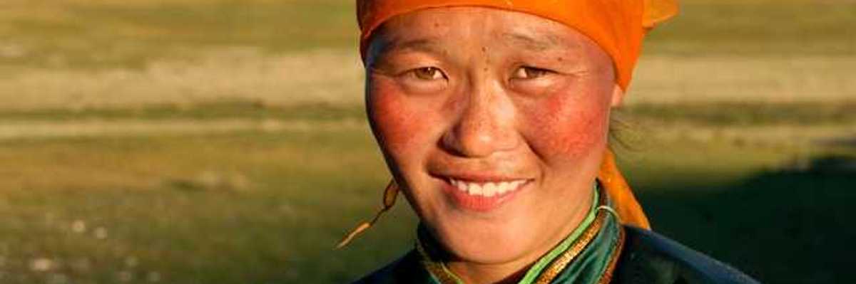 A Mongolian woman wearing an orange scarf on her head looking into the camera