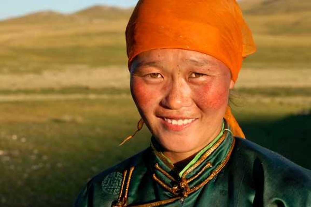 A Mongolian woman wearing an orange scarf on her head looking into the camera