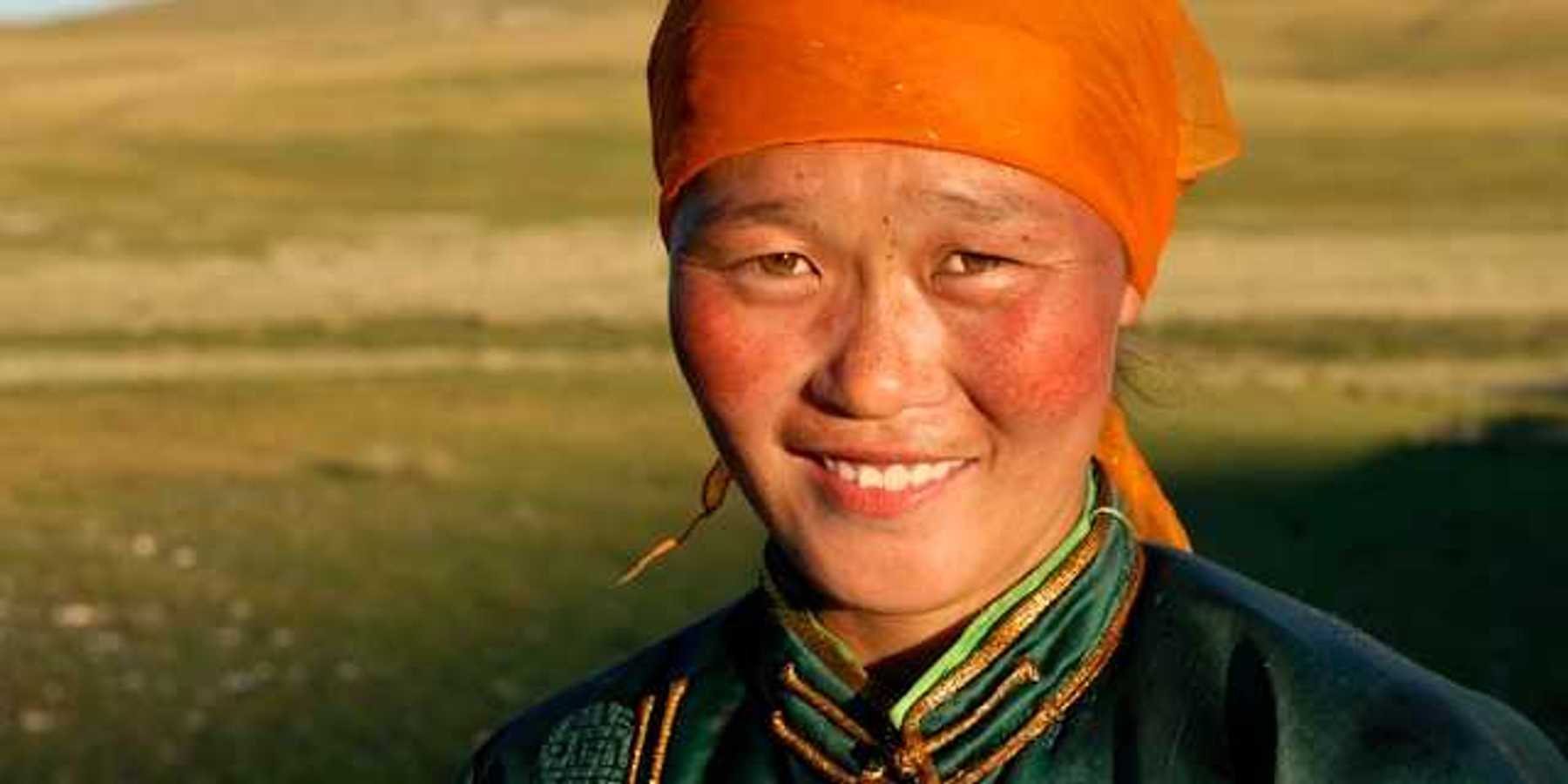 A Mongolian woman wearing an orange scarf on her head looking into the camera