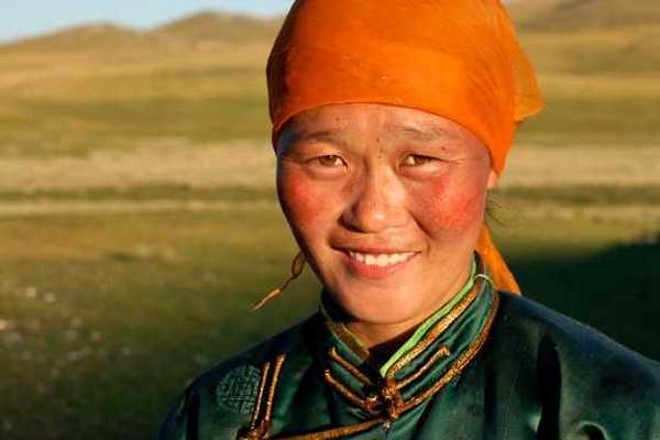 A Mongolian woman wearing an orange scarf on her head looking into the camera