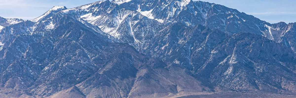 a mountain range with light snow and a desert environment in the foreground