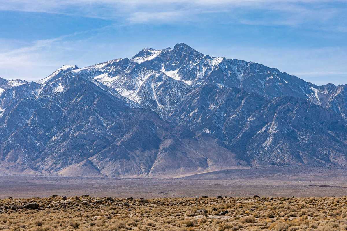 a mountain range with light snow and a desert environment in the foreground