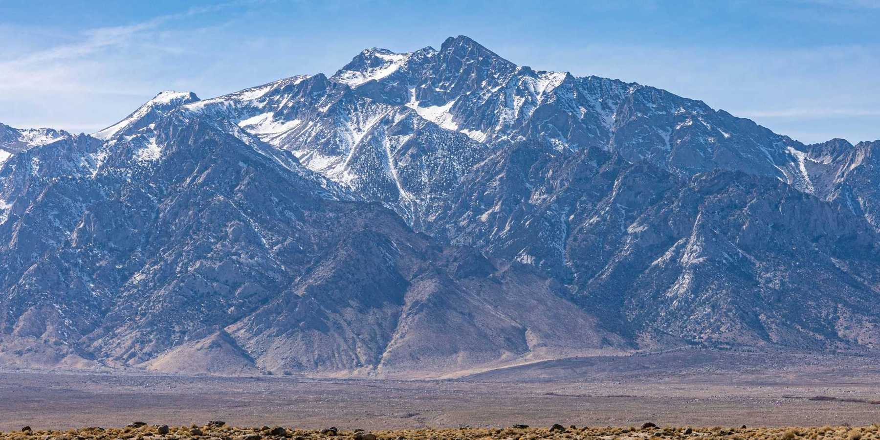 a mountain range with light snow and a desert environment in the foreground