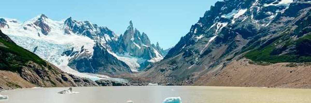 A mountain range with snow in front of a glacial lake with melting glaciers