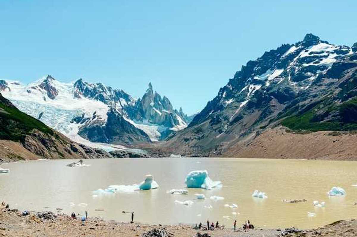 A mountain range with snow in front of a glacial lake with melting glaciers