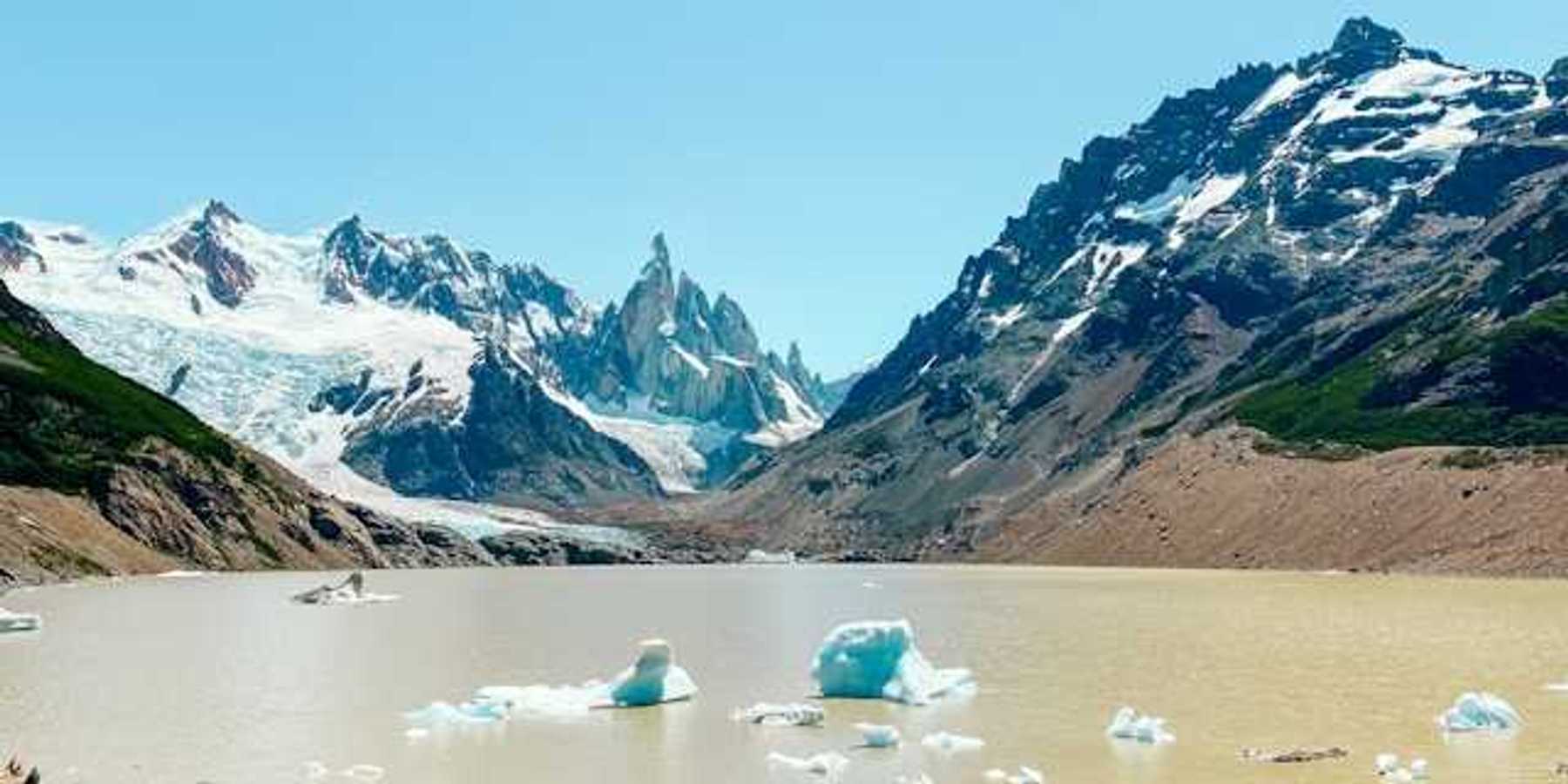 A mountain range with snow in front of a glacial lake with melting glaciers