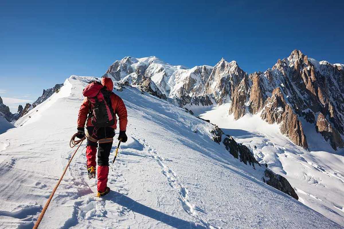A mountaineer climbs a snowy Mont Blanc in red snow gear