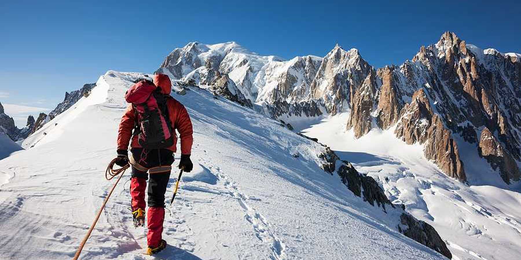 A mountaineer climbs a snowy Mont Blanc in red snow gear