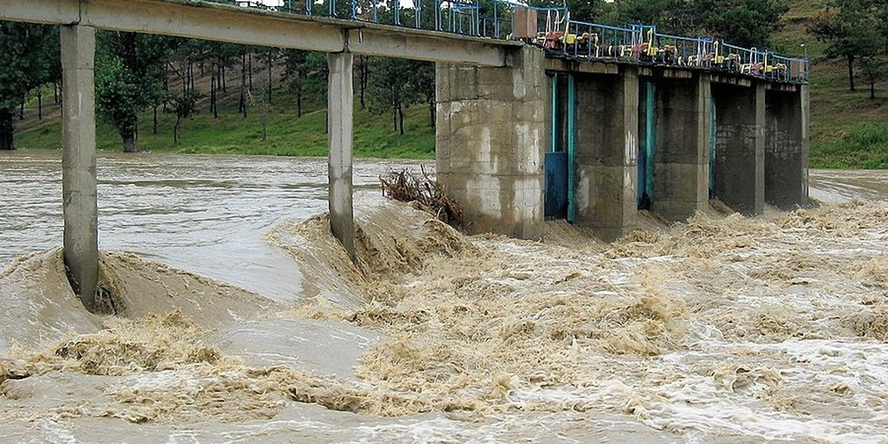 A narrow concrete bridge with fast flood waters streaming below it.