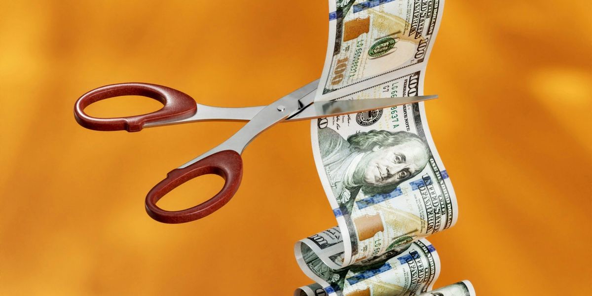 A pair of scissors cuts through a sequence of 100 dollar bills.