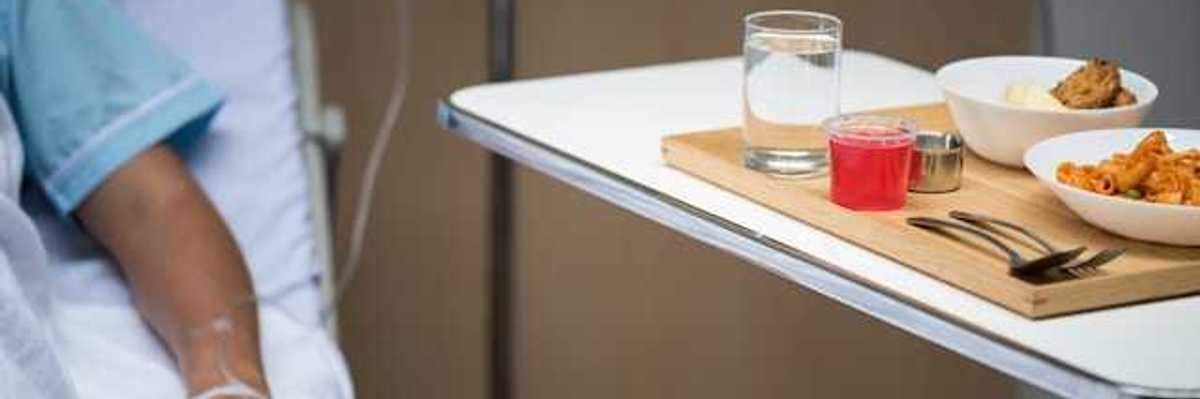 A patient sitting in a hospital bed next to a table with a meal