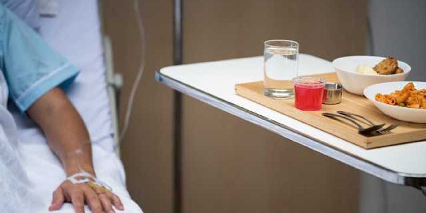 A patient sitting in a hospital bed next to a table with a meal