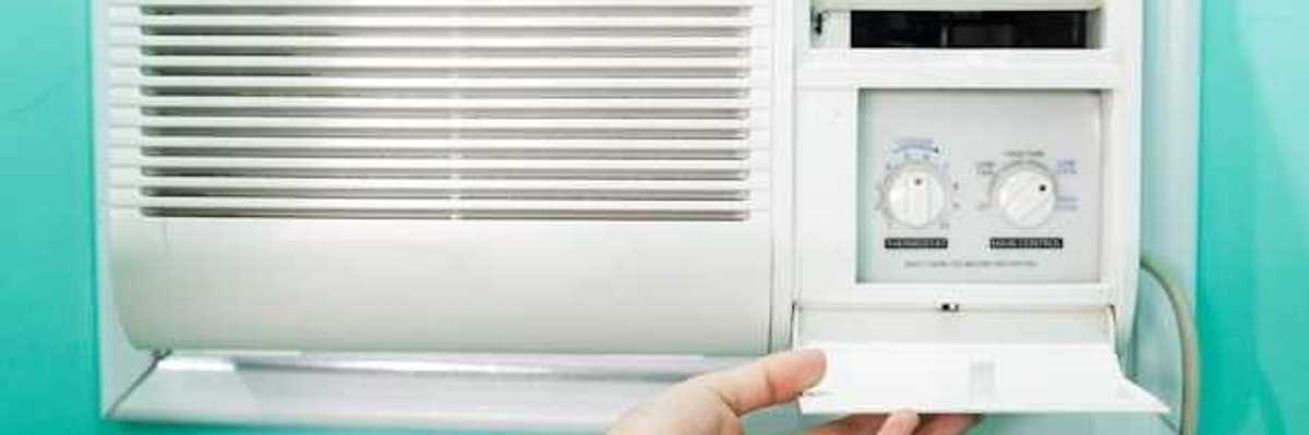 A person adjusting the controls on a window air conditioning unit