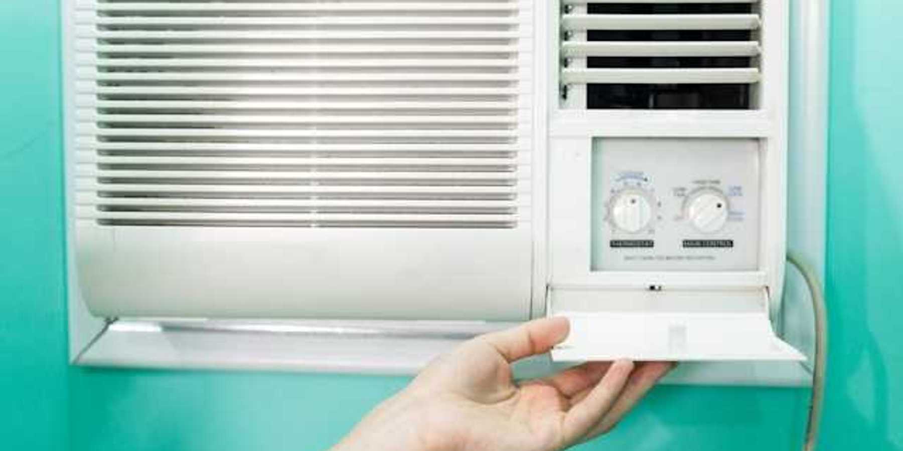 A person adjusting the controls on a window air conditioning unit