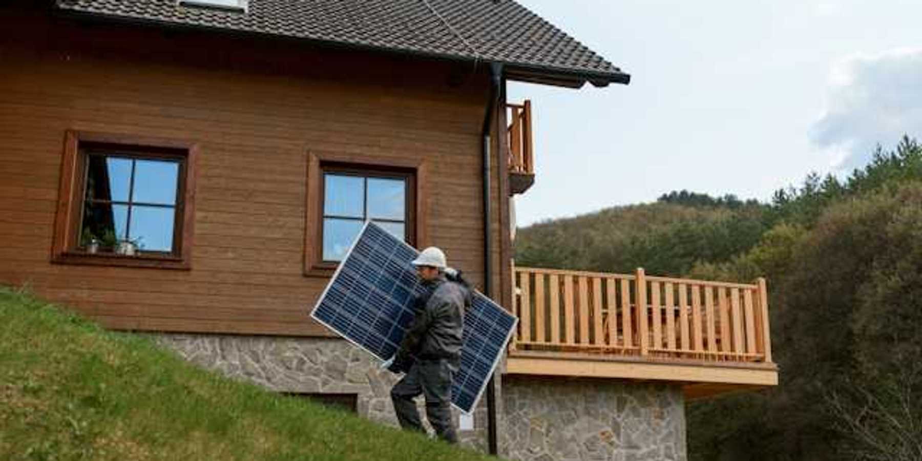 A person carrying a solar panel past a house