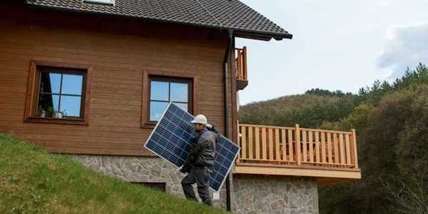 A person carrying a solar panel past a house