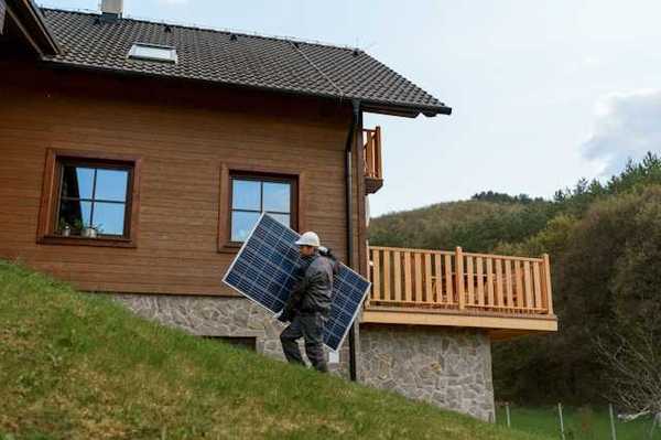 A person carrying a solar panel past a house