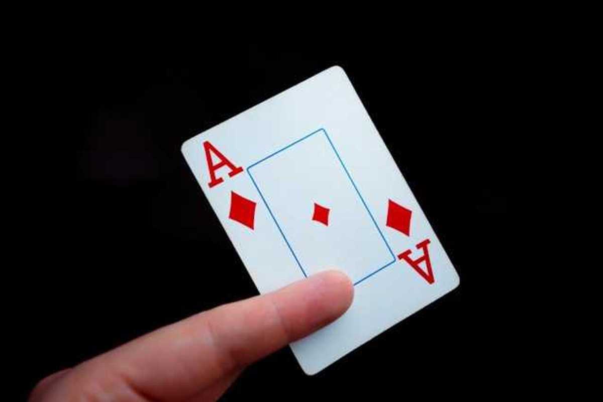 A person holding a card with the ace of diamonds on it