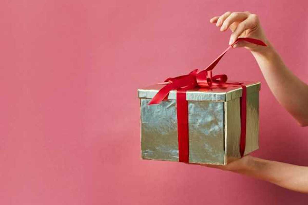 A person holding a gold-wrapped gift against a pink screen