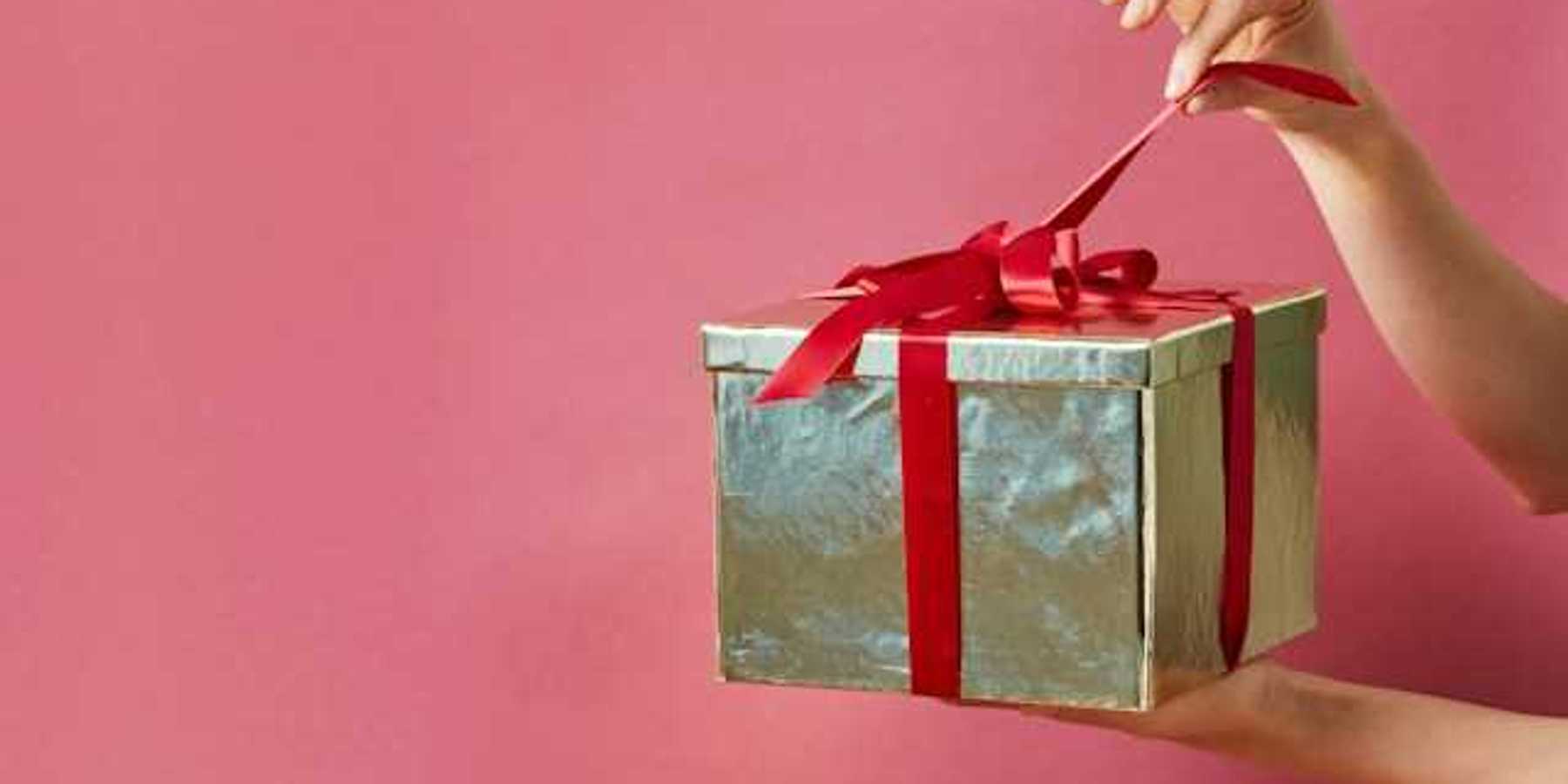 A person holding a gold-wrapped gift against a pink screen