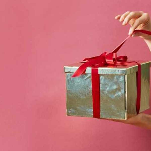 A person holding a gold-wrapped gift against a pink screen