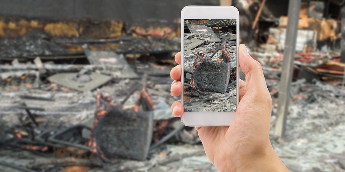 A person holding a mobile phone taking a photo of a burned home
