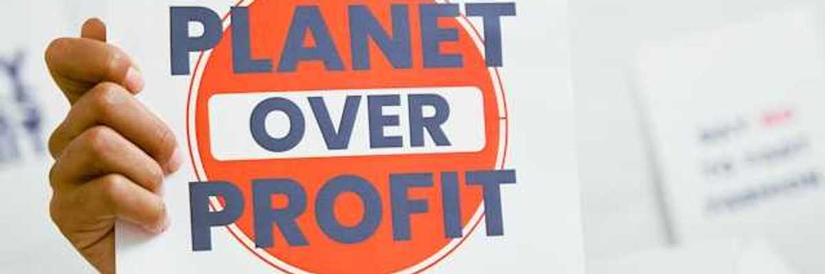 A person holding a sign that says Planet Over Profit