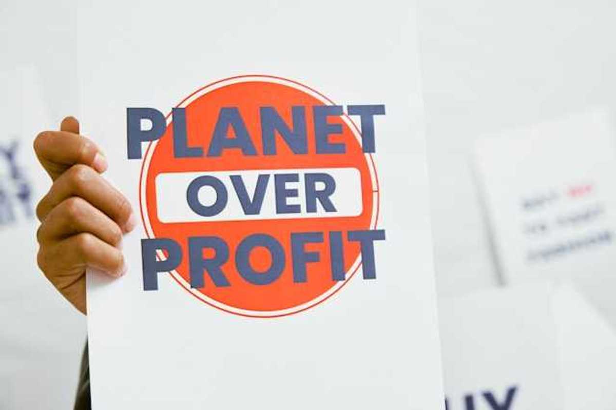 A person holding a sign that says Planet Over Profit