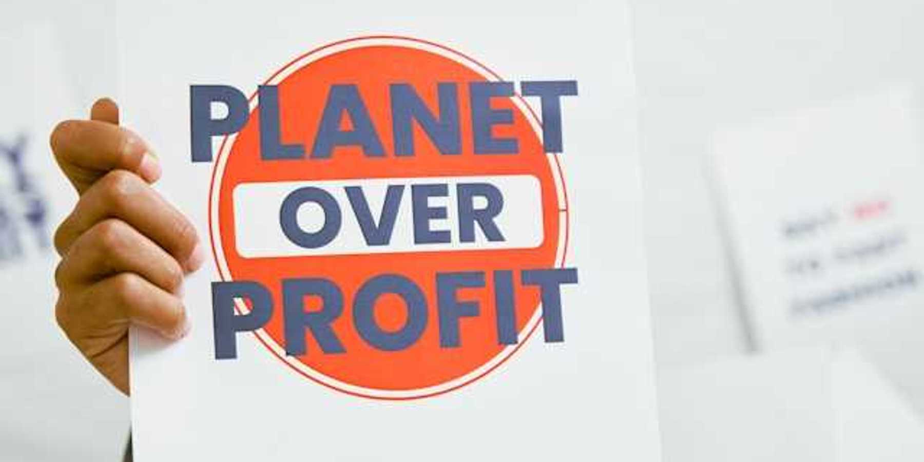 A person holding a sign that says Planet Over Profit