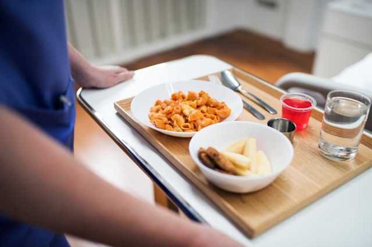 A person holding a tray with a hospital meal on it